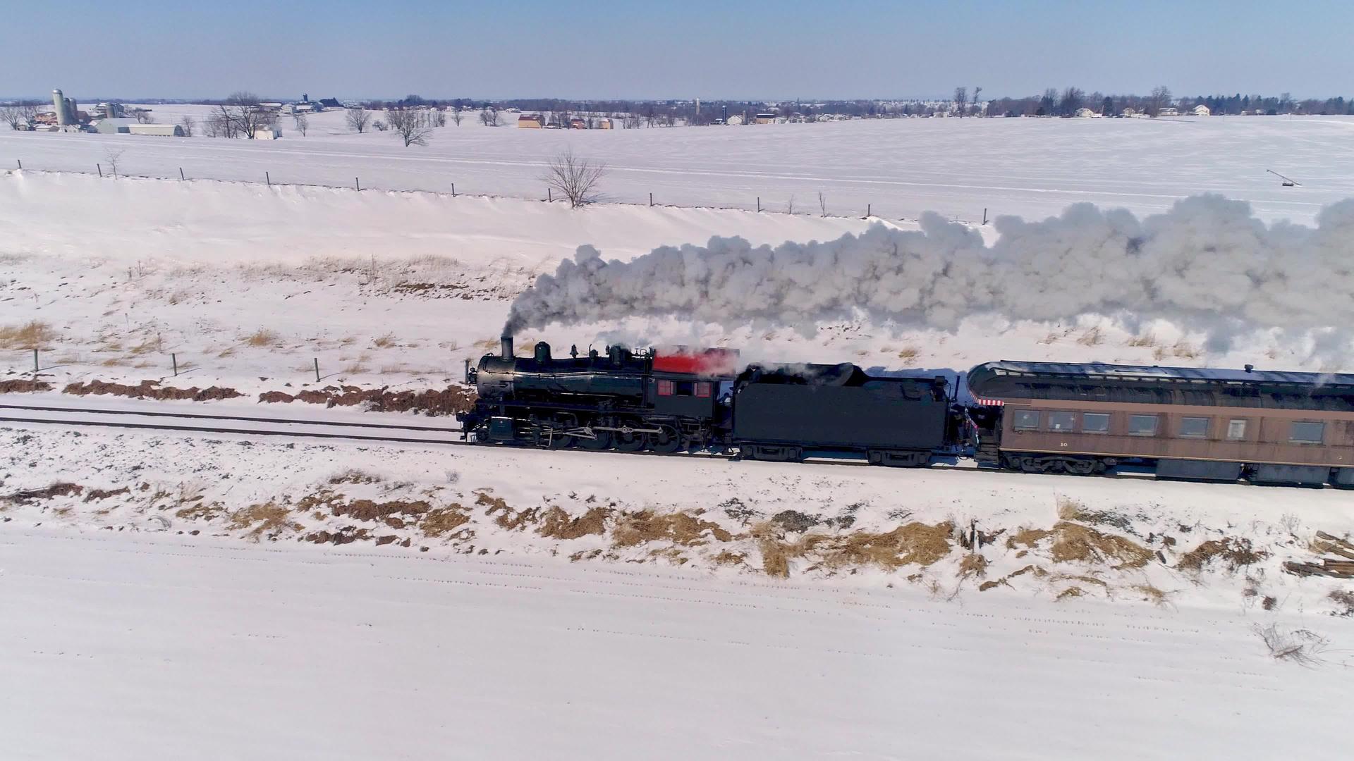 看到古老的蒸汽机车接近并拉着公共汽车在暴风雪后吹起烟雾和烟雾视频的预览图