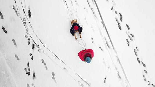 母亲在新鲜的雪地上用雪橇拉着孩子从上面可以看到脚印视频的预览图