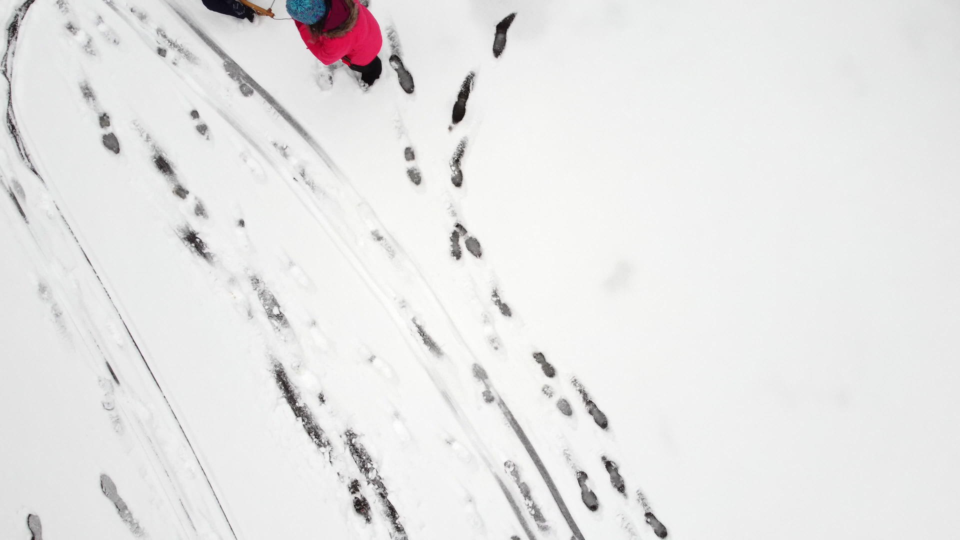 母亲在新鲜的雪地上用雪橇拉着孩子从上面可以看到脚印视频的预览图