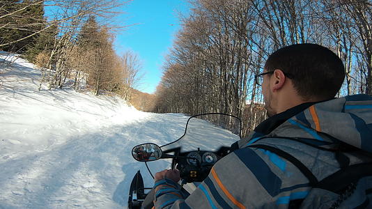在阳光明媚的一天一名男子驾驶一辆运动车在森林里骑雪地视频的预览图