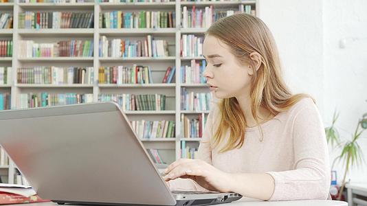 迷人的女孩在图书馆的电脑上工作写着视频的预览图