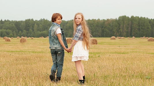 这对年轻夫妇手牵手走在干草堆背景下的乡村田野上视频的预览图