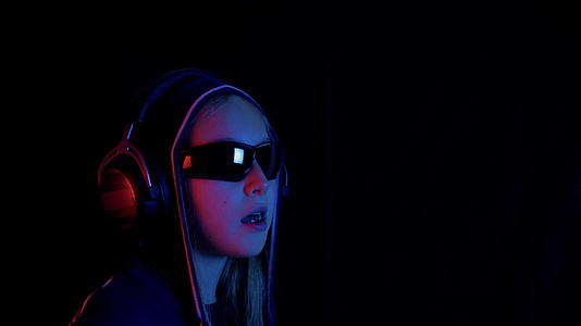 戴着口袋帽和黑色太阳镜的女孩在黑暗的房间里使用红色和蓝色视频的预览图