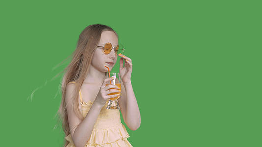 十几岁的女孩用吸管从透明的绿色背景玻璃上喝橙汁视频的预览图