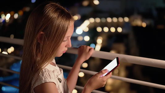 十几岁的女孩在黑暗的阳台上的社交网络中使用智能手机视频的预览图