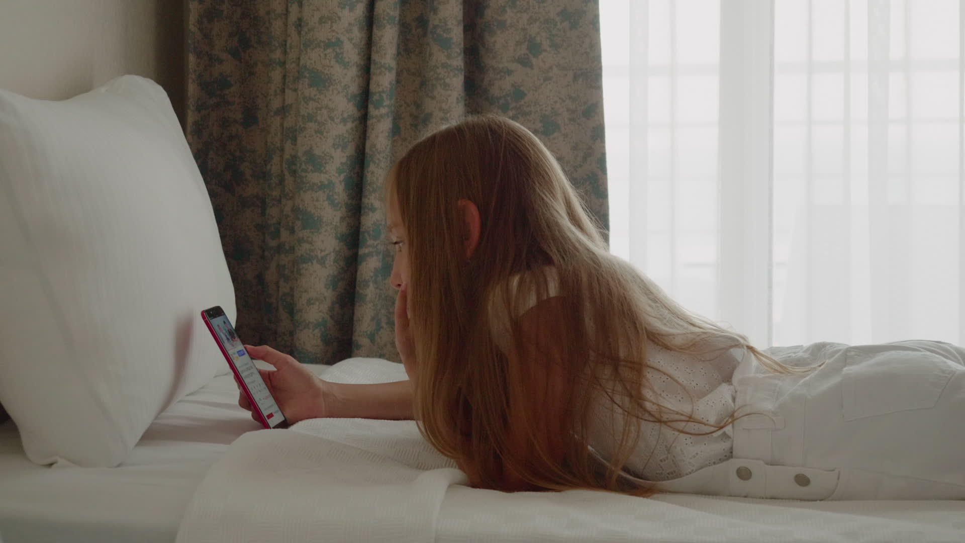 可爱可爱的女孩躺在床上留着长发使用智能手机视频的预览图
