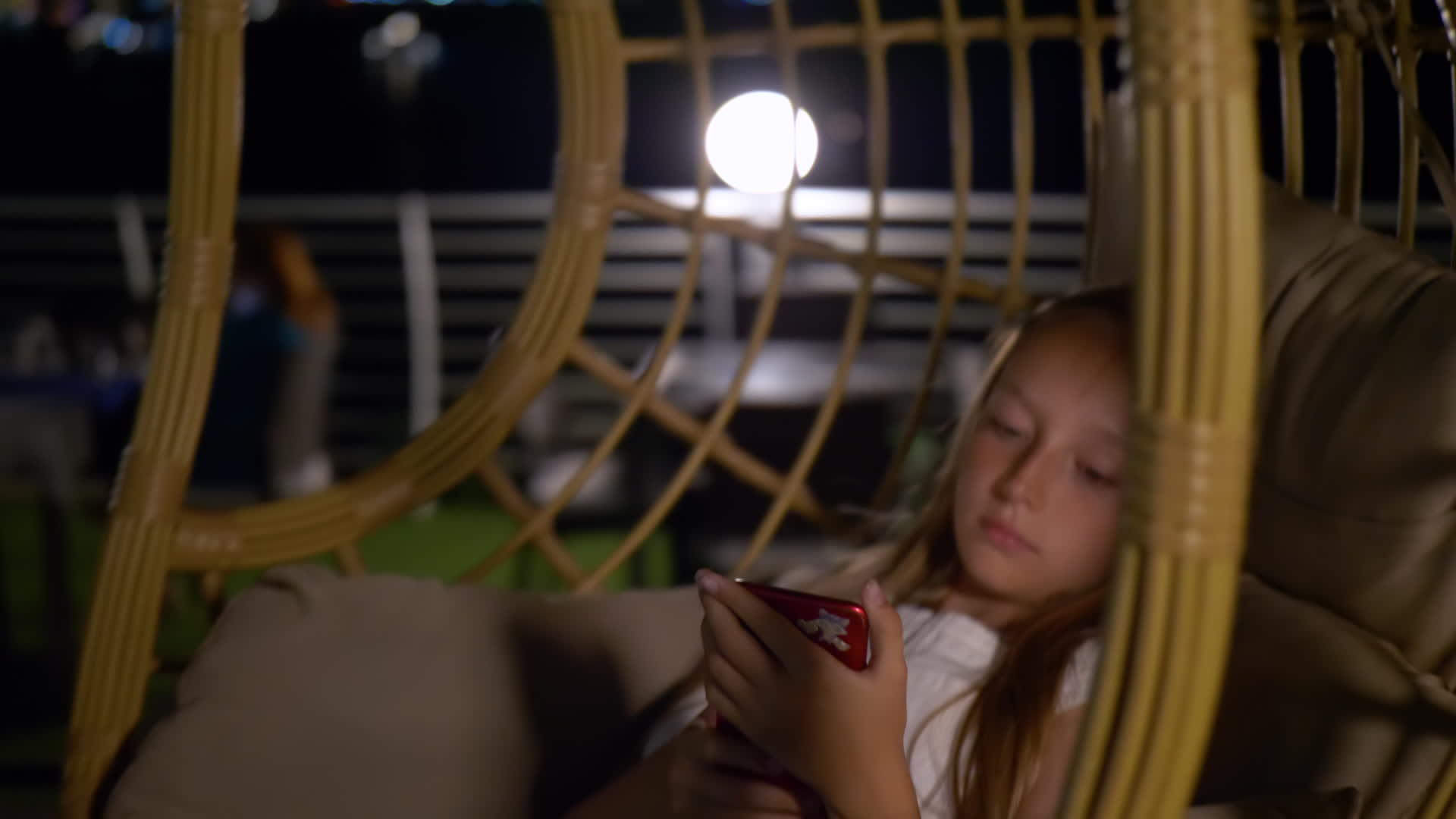十几岁的女孩正在寻找智能手机的茧椅上荡秋千视频的预览图
