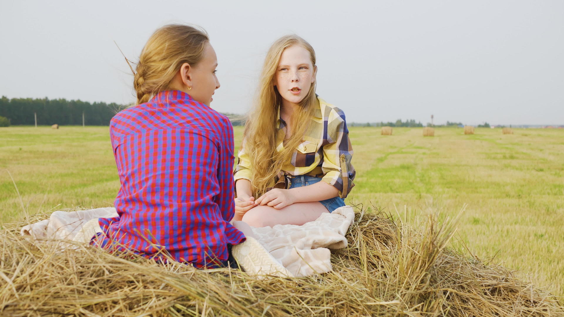 十几岁的女孩朋友坐在村里农田的干草堆上视频的预览图