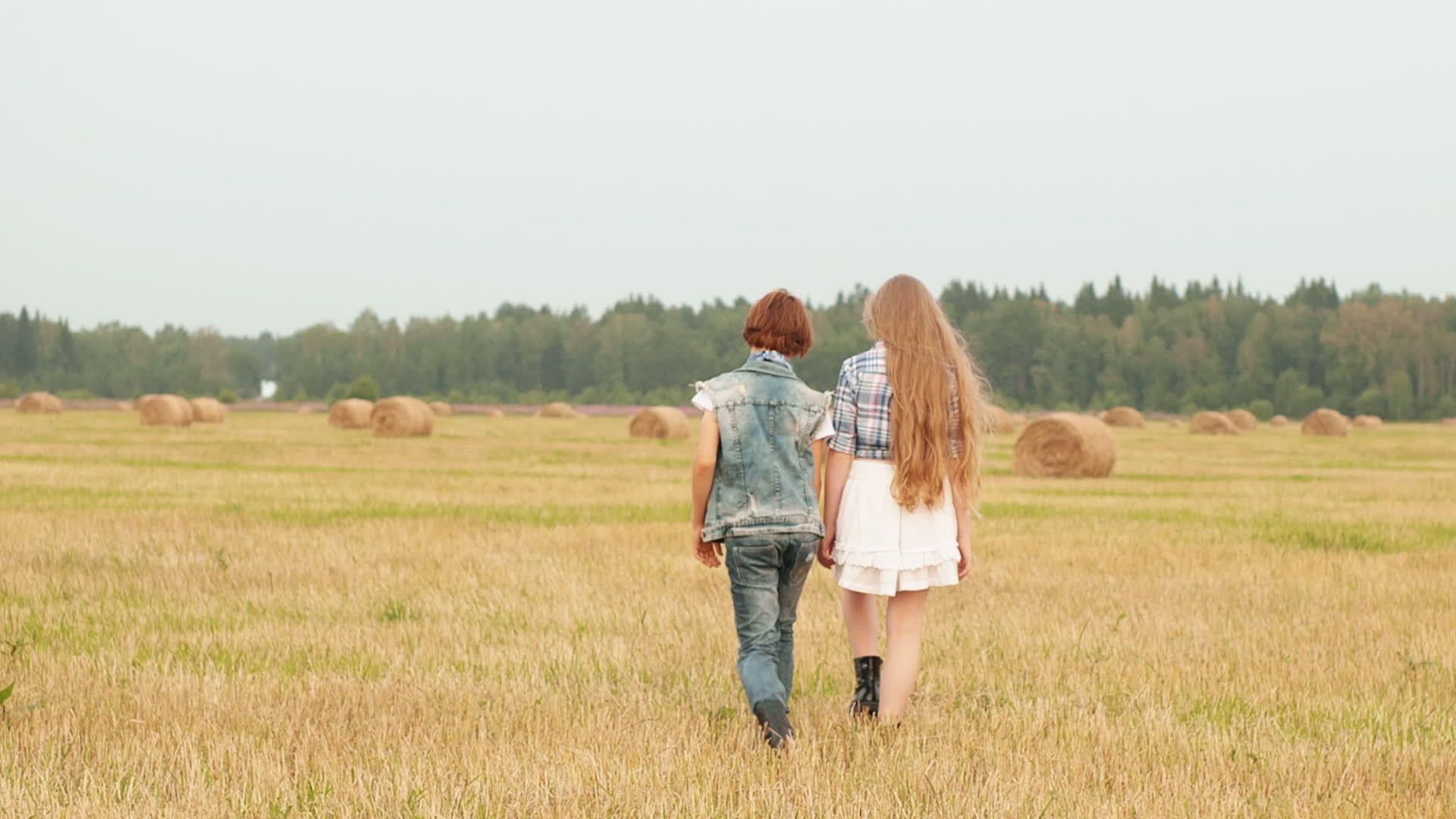 十几岁的女孩和男孩在草堆背景下的收割场上快乐地走着视频的预览图