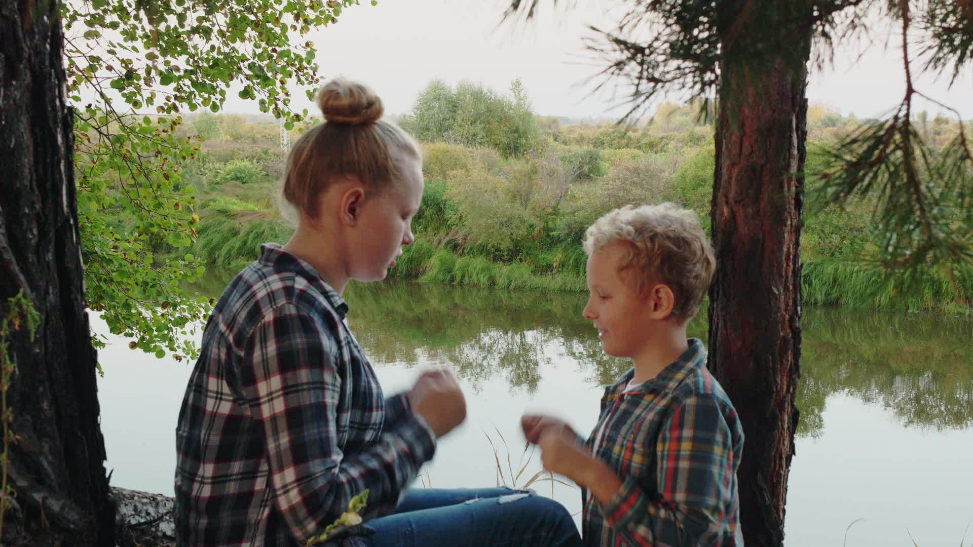 十几岁的女孩和男孩在松树林的河岸上玩剪刀、石头和布视频的预览图