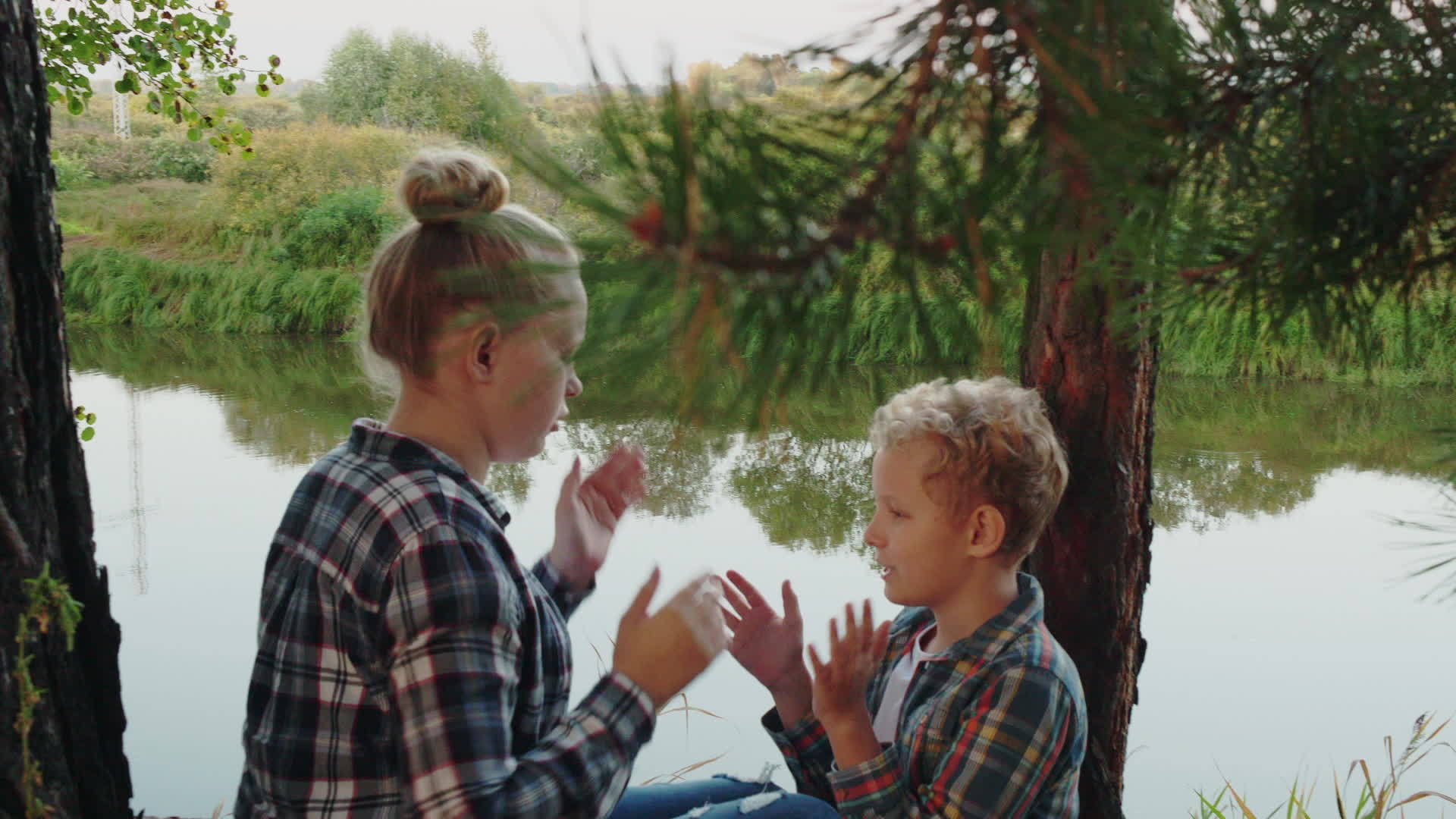 十几岁的女孩和男孩在针叶林的河岸上快乐地玩帕蒂蛋糕视频的预览图
