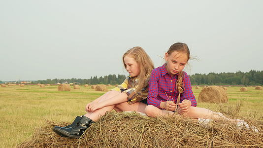 十几岁的女孩坐在高峰干草堆上严肃的女孩在收割场上视频的预览图