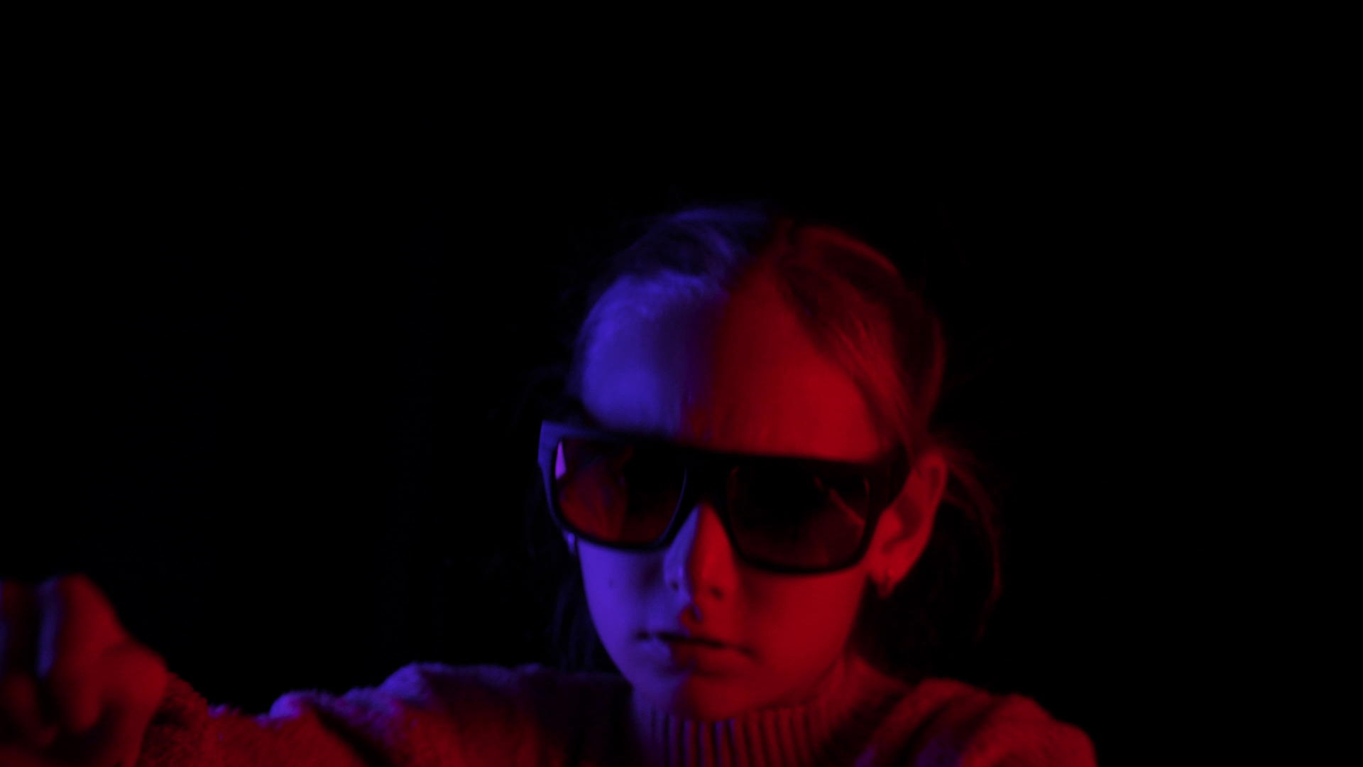 戴着深色太阳镜的女孩在黑色背景上使用蓝色和红色的灯视频的预览图