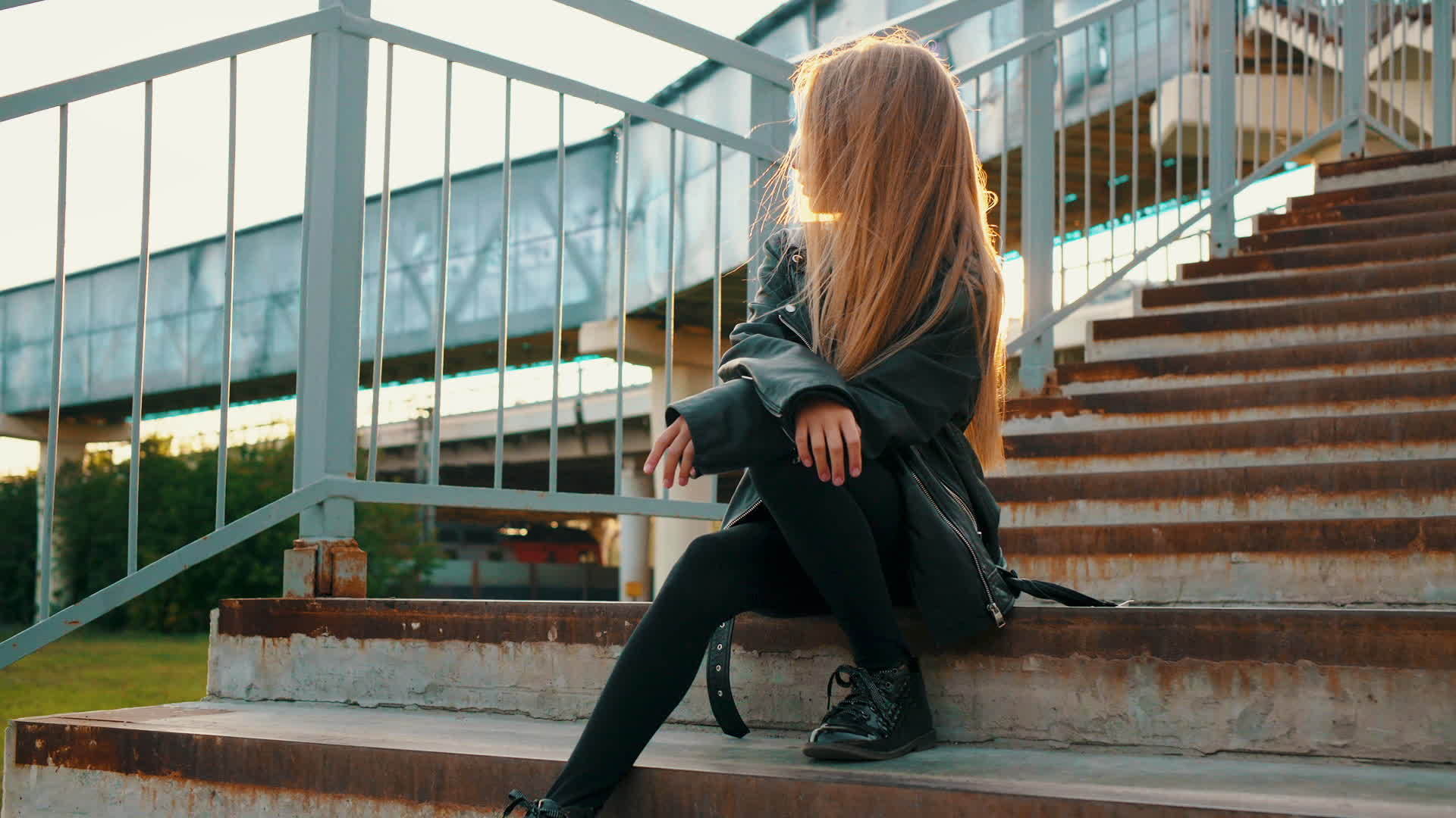 一个穿着黑色皮夹克的女孩坐在城市景观的楼梯上视频的预览图