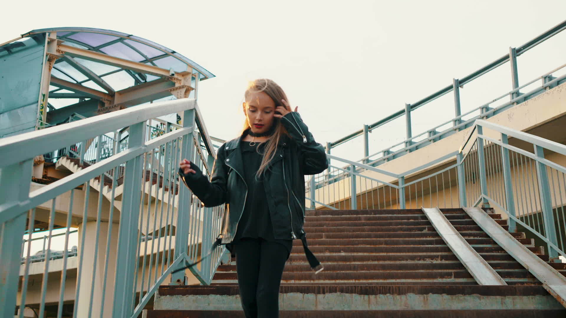 在城市的背景下穿着黑色皮夹克的女孩走下楼梯穿着皮夹克视频的预览图