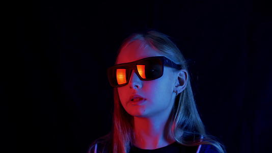 戴着黑色太阳镜的女孩在霓虹灯的黑暗房间里嚼着口香糖视频的预览图