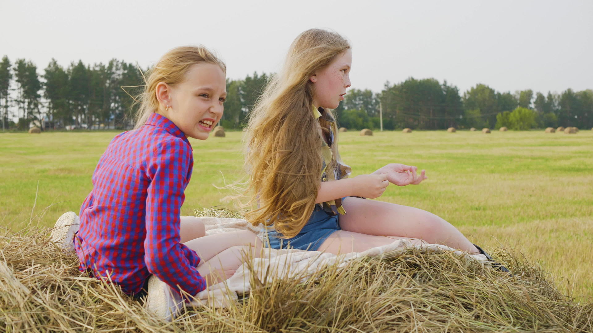 两个十几岁的女孩坐在农田的干草堆上视频的预览图