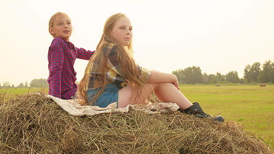 两个女孩坐在村里收割场顶层的干草堆上视频的预览图