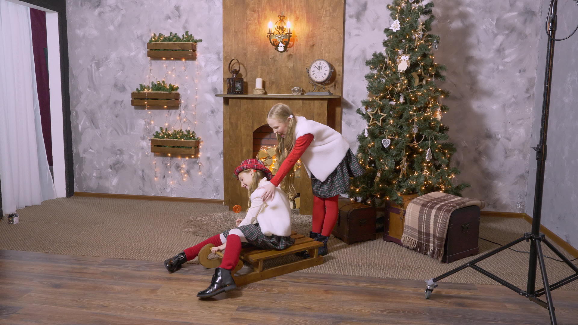 穿着棒棒糖的女孩在雪橇上穿着圣诞树背景的衣服视频的预览图