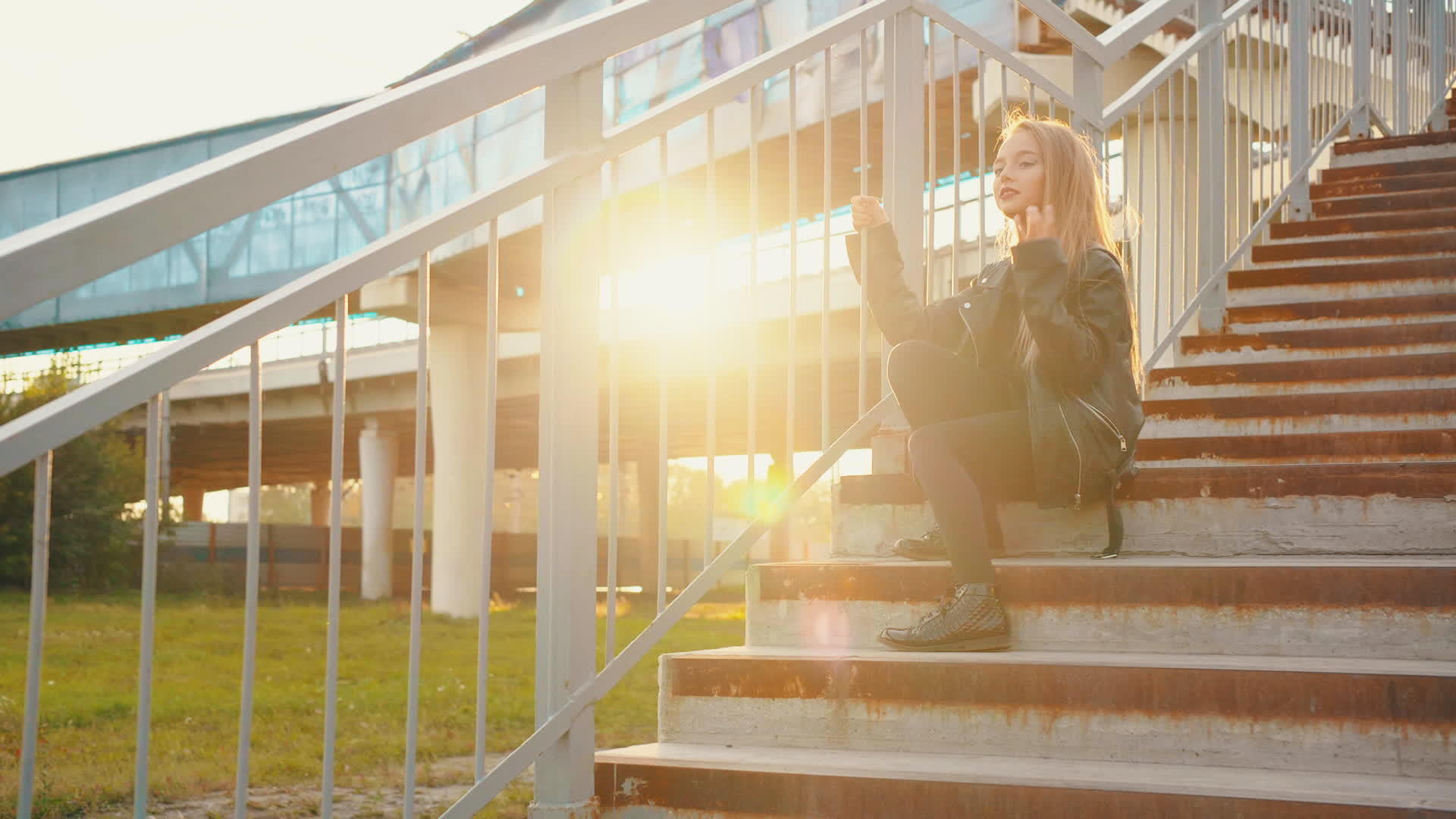 一个穿着黑色皮夹克的女孩坐在阳光背景的楼梯上视频的预览图