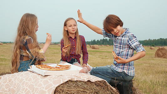 年轻的女孩和男孩在收割场的干草堆上吃披萨视频的预览图