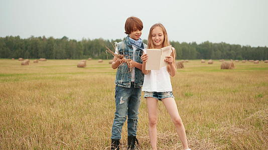 十几岁的男孩和女孩在干草堆景观中阅读关于收割场的书籍视频的预览图