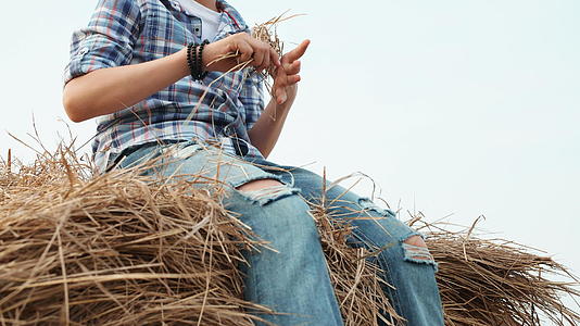 十几岁的男孩穿着牛仔裤和格子衬衫坐在农村的干草堆上视频的预览图