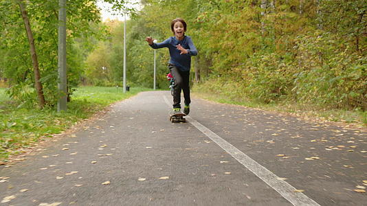 十几岁的男孩在公园路上骑滑板小男孩在公园里骑秋天视频的预览图