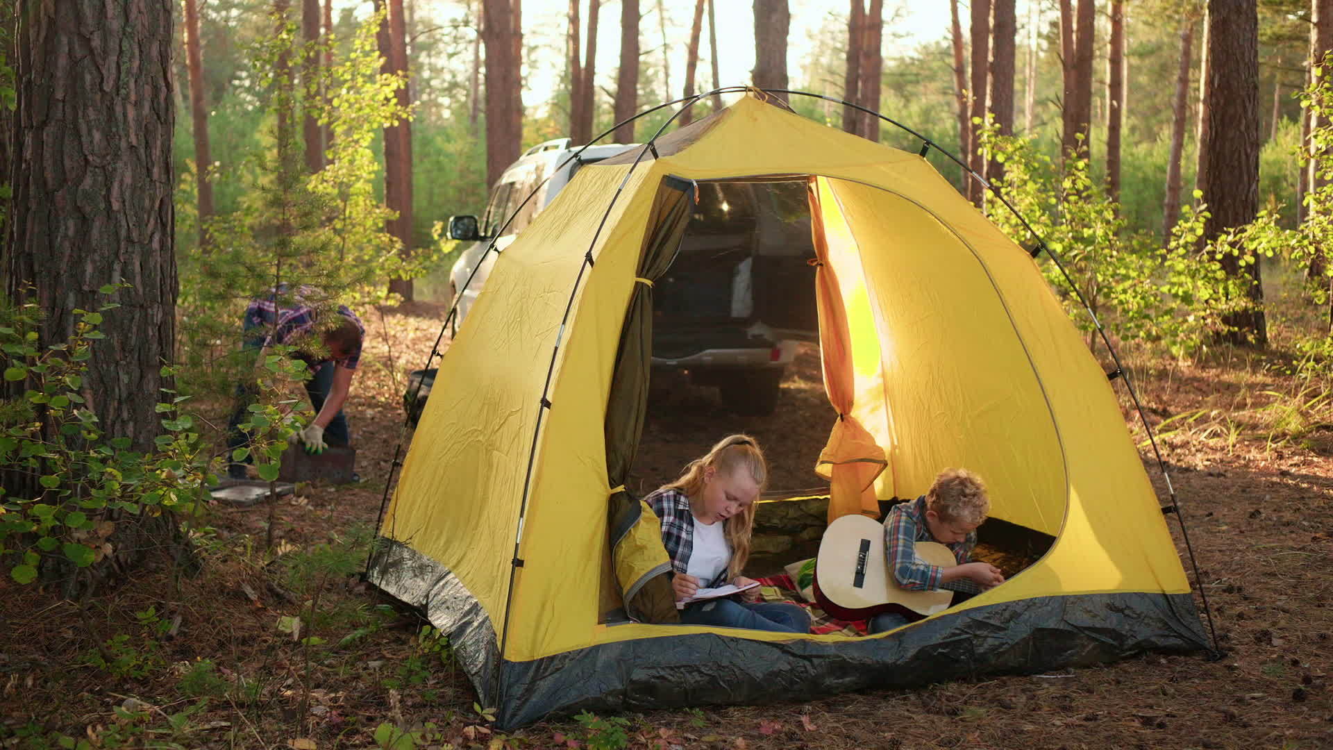 十几岁的男孩在阳光明媚的森林露营帐篷里用吉他演奏音乐视频的预览图