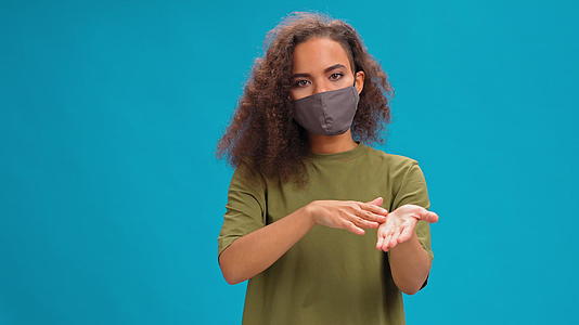 戴着保护面具的年轻女子看着镜头穿着橄榄t恤蓝色背景视频的预览图