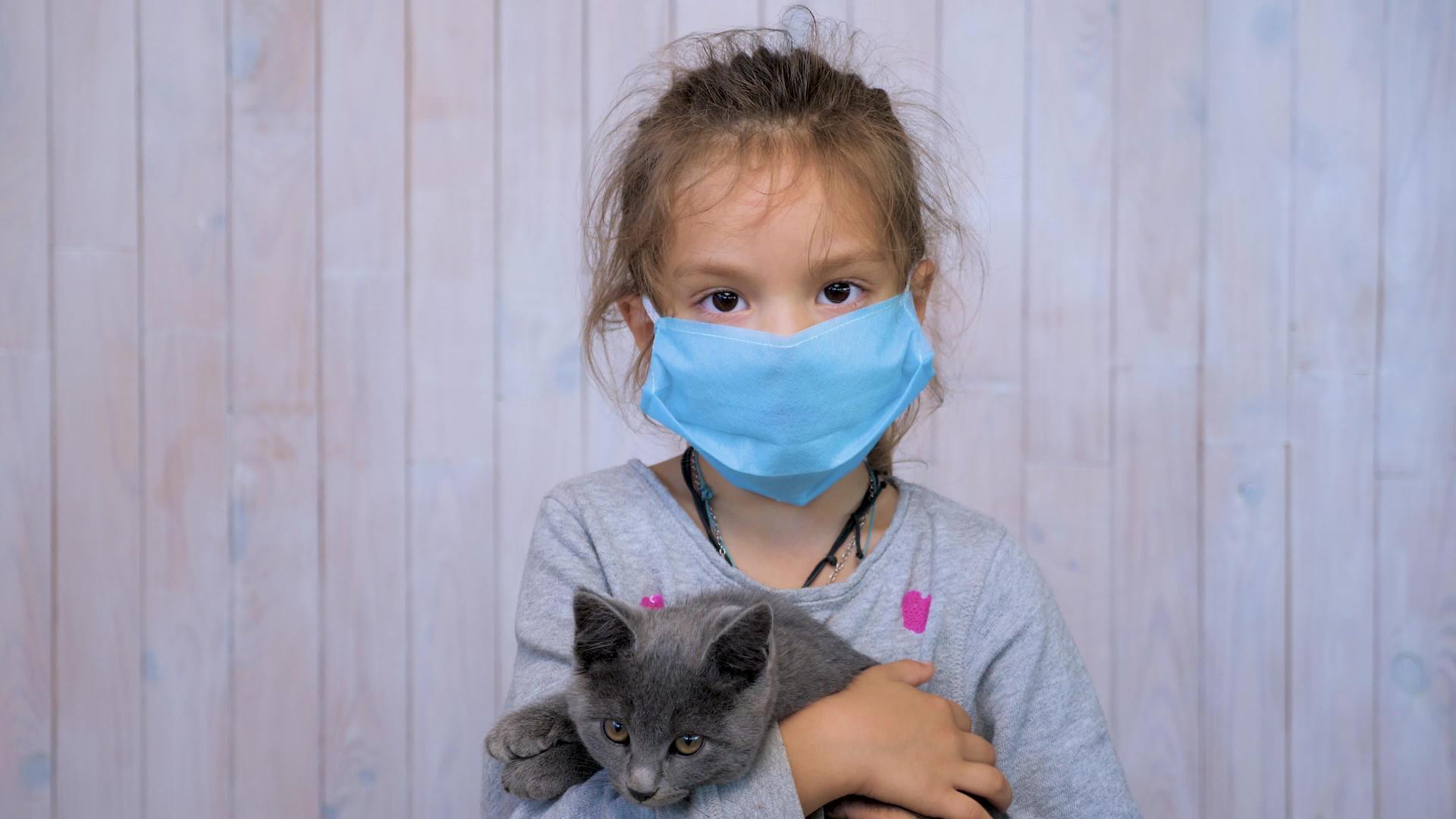 在大流行期间孩子们戴着医用面具手里拿着猫视频的预览图