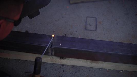 戴着防护口罩的年轻焊接工匠靠在工作台上焊接铁制品视频的预览图