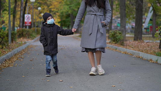 母亲和儿子戴着医用面具在公园里散步视频的预览图