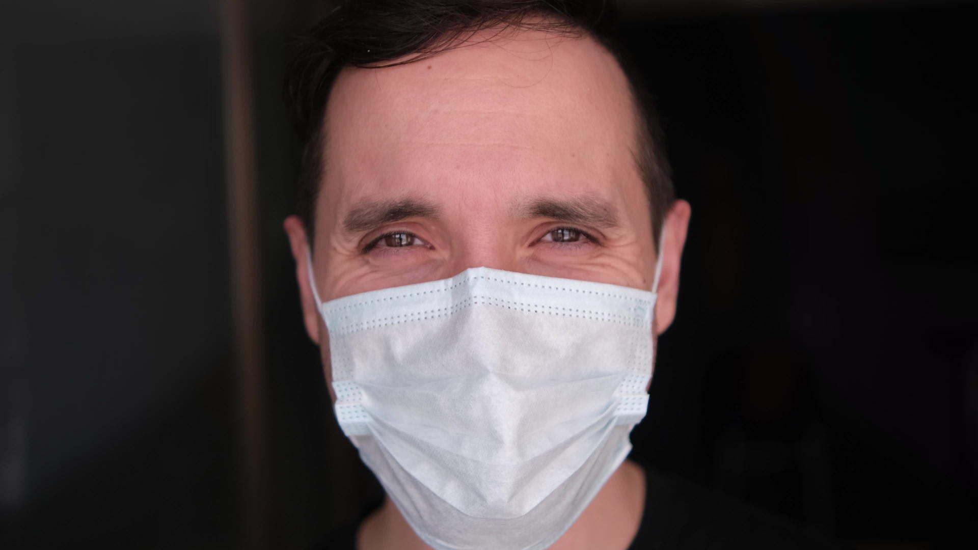 一个戴着医用口罩的年轻人穿着黑色t恤站在黑暗中视频的预览图