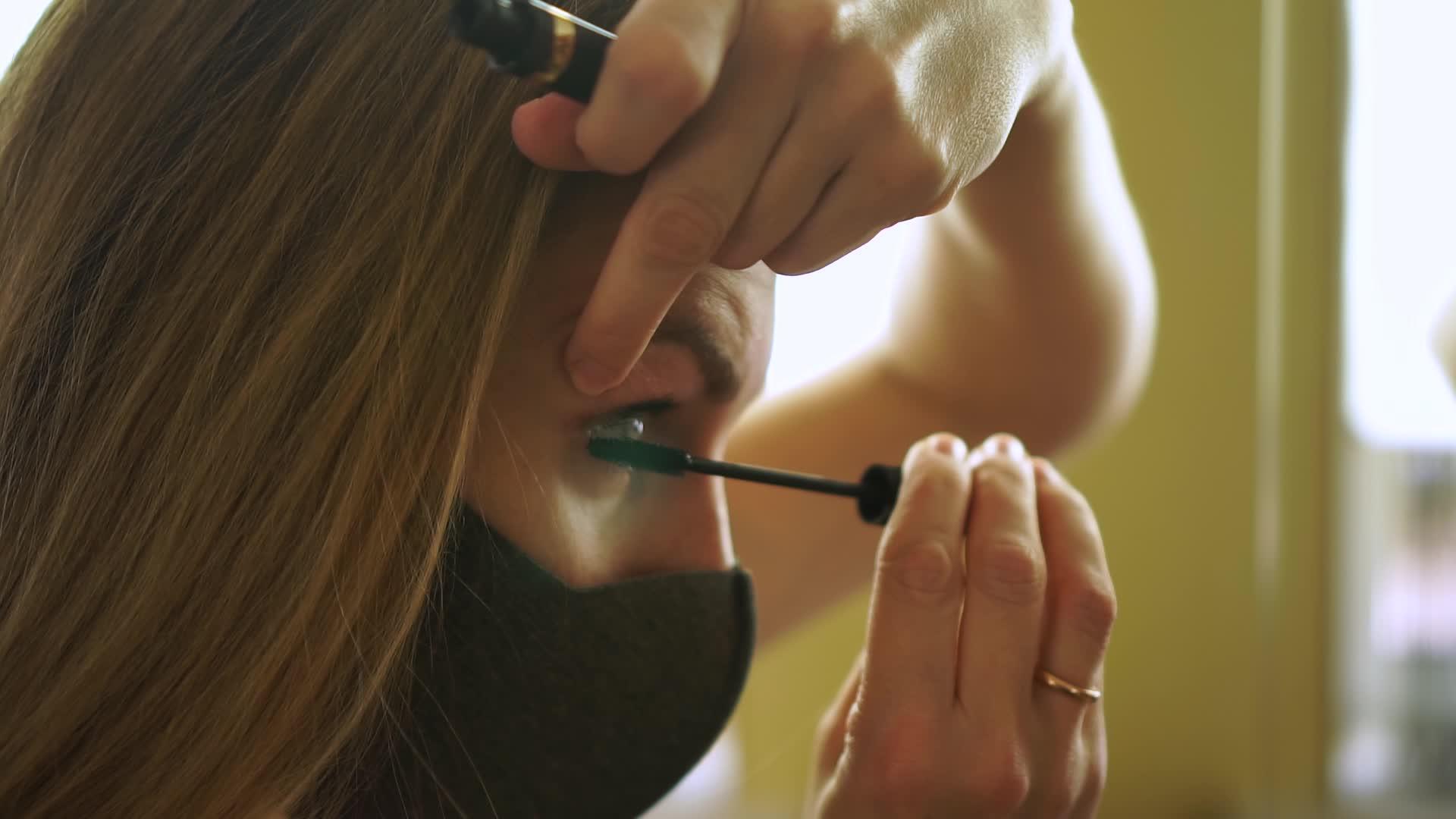 在检疫期间戴着黑色保护面具的年轻女性进行眼部化妆视频的预览图