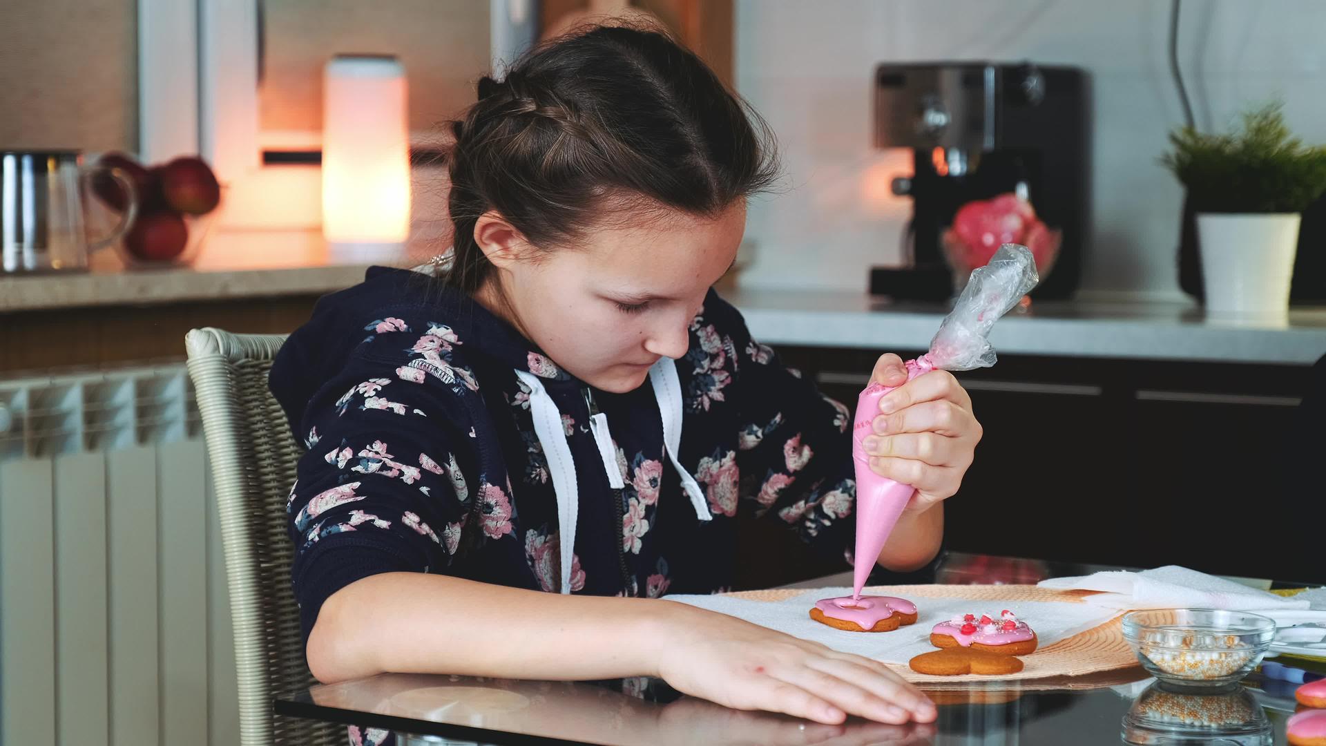 晚上漂亮的女孩在家里装饰着彩色糖霜饼干视频的预览图