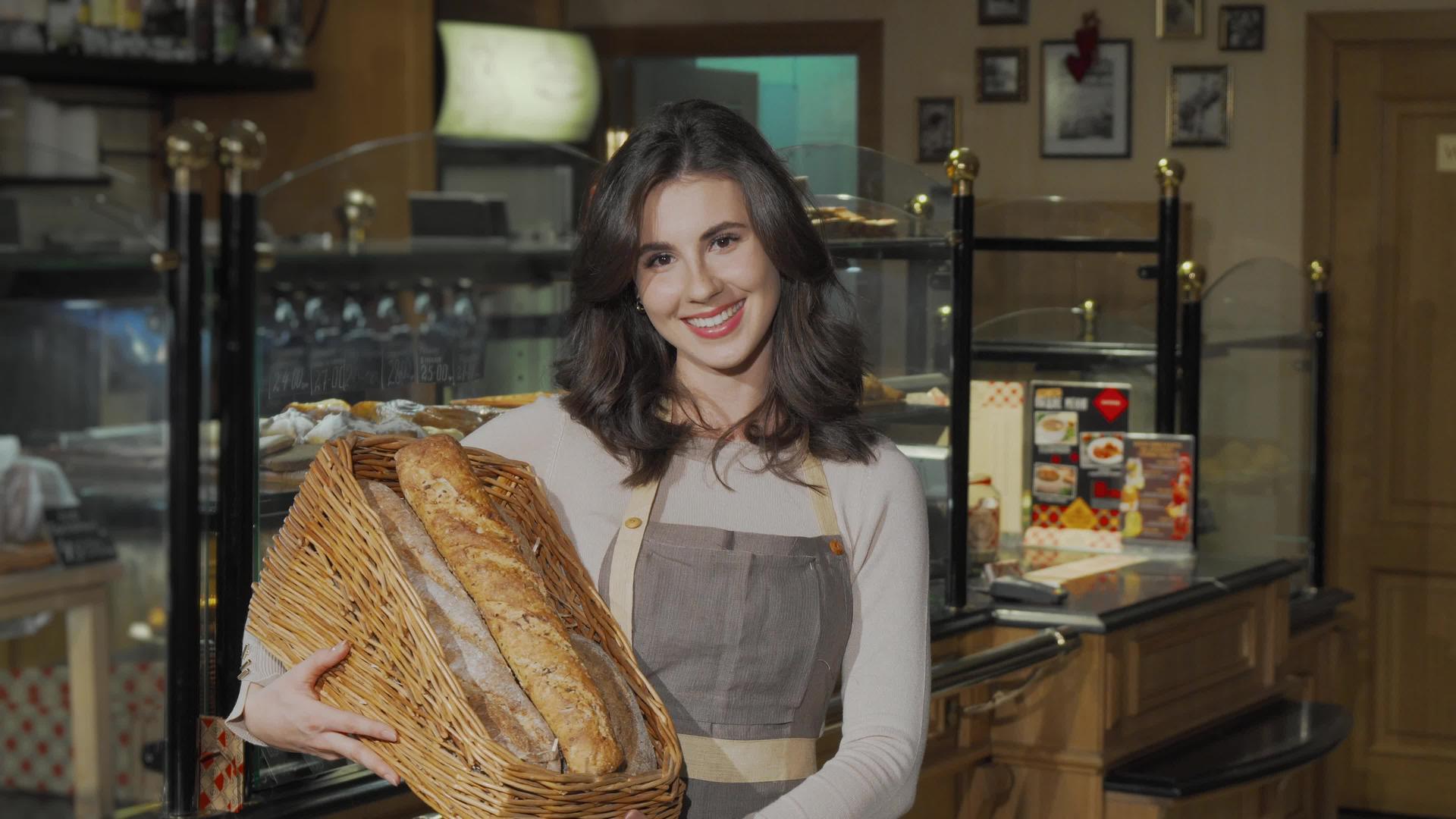 快乐的女面包师拿着新鲜的面包篮子对着相机微笑视频的预览图