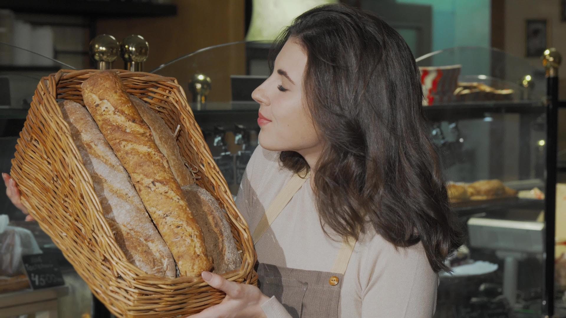 美丽的女面包师闻到了面包店卖的美味新鲜面包的味道视频的预览图
