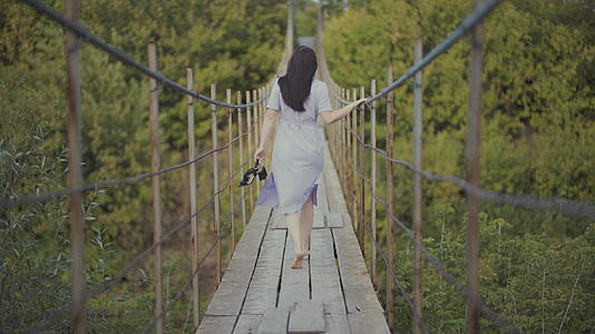 一个穿着漂亮裙子的女人在树林里的一座桥上奔跑女孩手里拿着一个女孩视频的预览图
