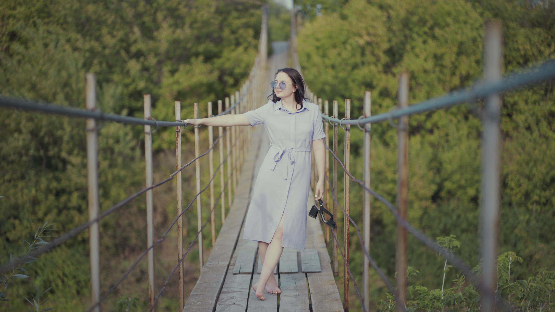 一个穿着漂亮裙子的女人站在树林里的一座桥上女孩手里拿着一个女孩视频的预览图