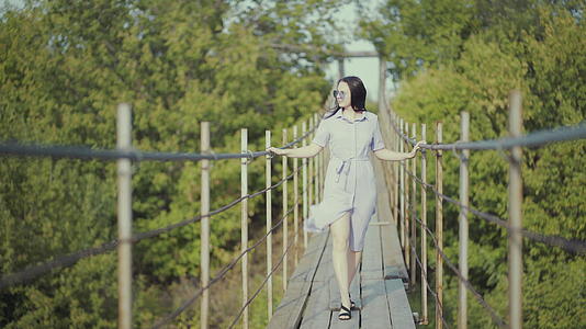 穿着漂亮裙子的女人在树林里的桥上散步视频的预览图