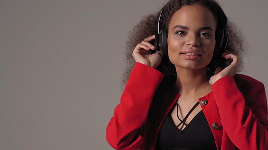 年轻快乐的非洲美国女孩在耳机里听音乐穿着红色夹克和黑色夹克视频的预览图