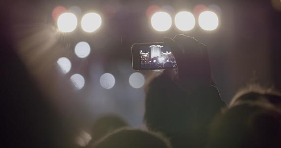 在户外音乐会上通过智能手机在明亮的聚光灯前录制舞台视频的预览图
