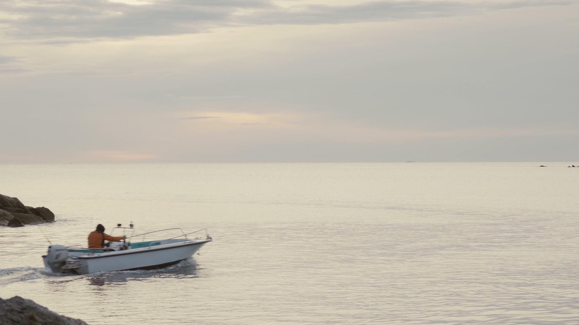 当日出或日落时充气船在阳光较低的平海上离开小港口视频的预览图