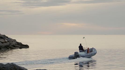 当日出或日落时充气船在阳光较低的平海上离开小港口视频的预览图