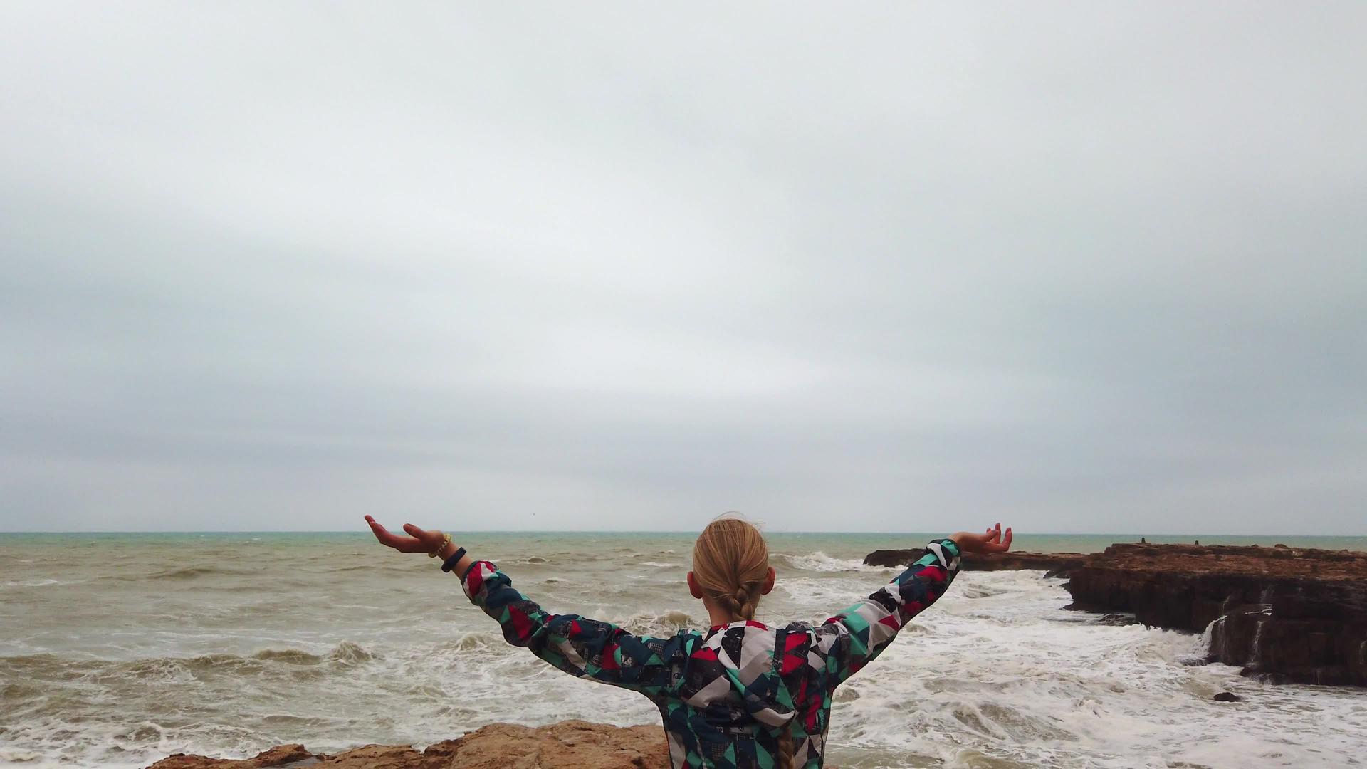 女孩举起手在暴风雨中与她一起站在海岸上视频的预览图