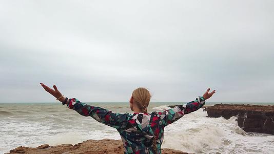 女孩举起手在暴风雨中与她一起站在海岸上视频的预览图