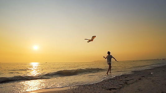 可爱的快乐男孩戴着帽子在海岸海滩上奔跑和玩风筝对抗充满活力的人视频的预览图