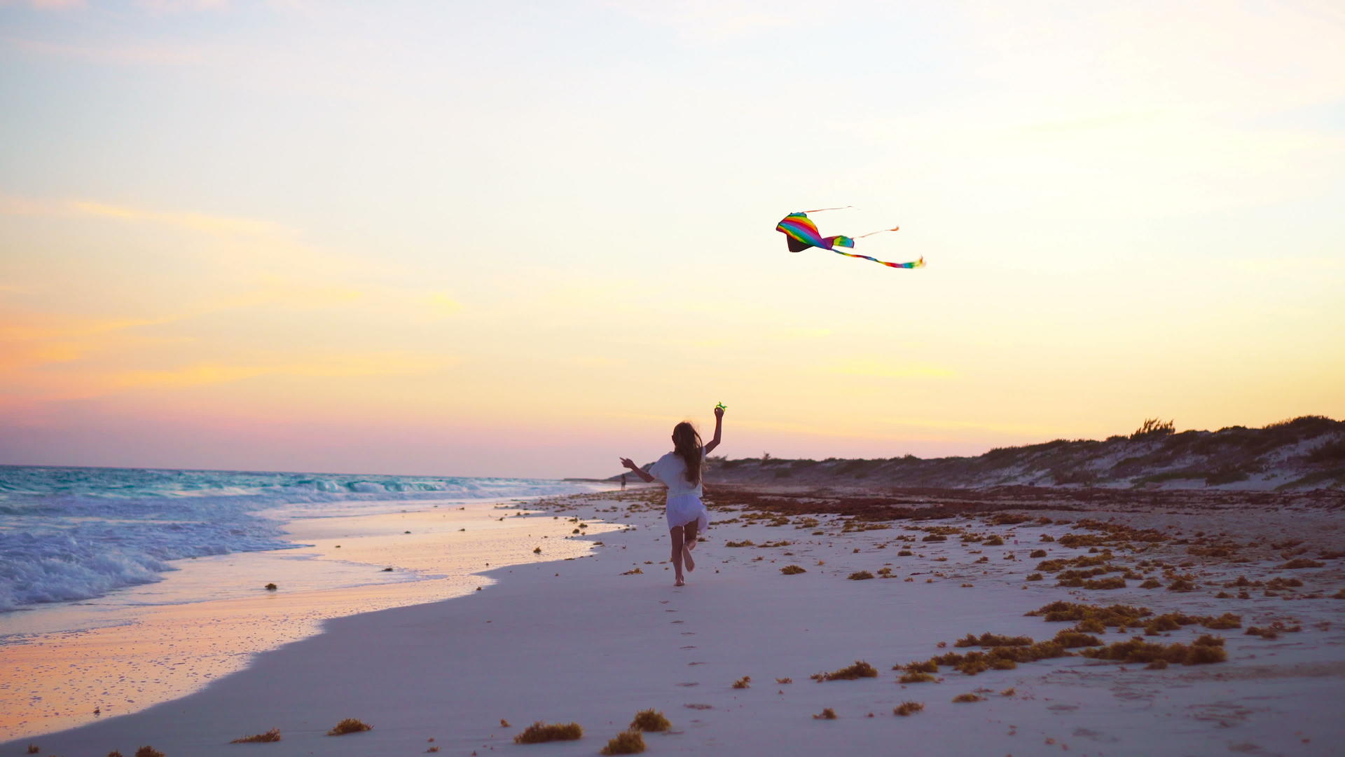日落时在热带海滩上放风筝的小跑女孩在海滩上玩耍视频的预览图