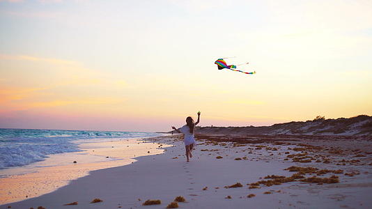 日落时在热带海滩上放风筝的小跑女孩在海滩上玩耍视频的预览图